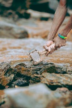 Person holding a rock hammer while examining a rock outcrop outdoors