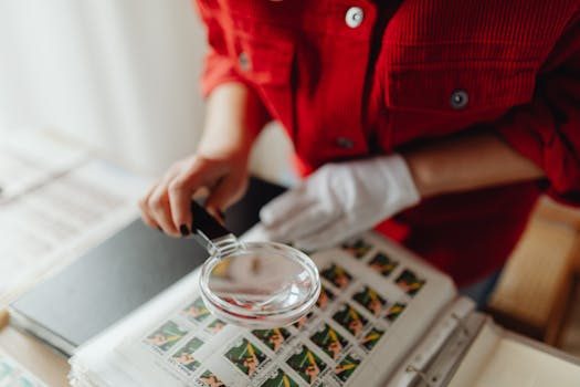 A vintage stamp album open on a wooden table with a magnifier resting on top of a page