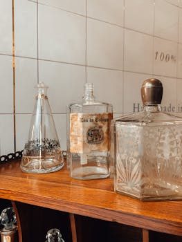 A curated collection of Art Deco and vintage perfume bottles displayed on a glass shelf, showing varied colors and shapes