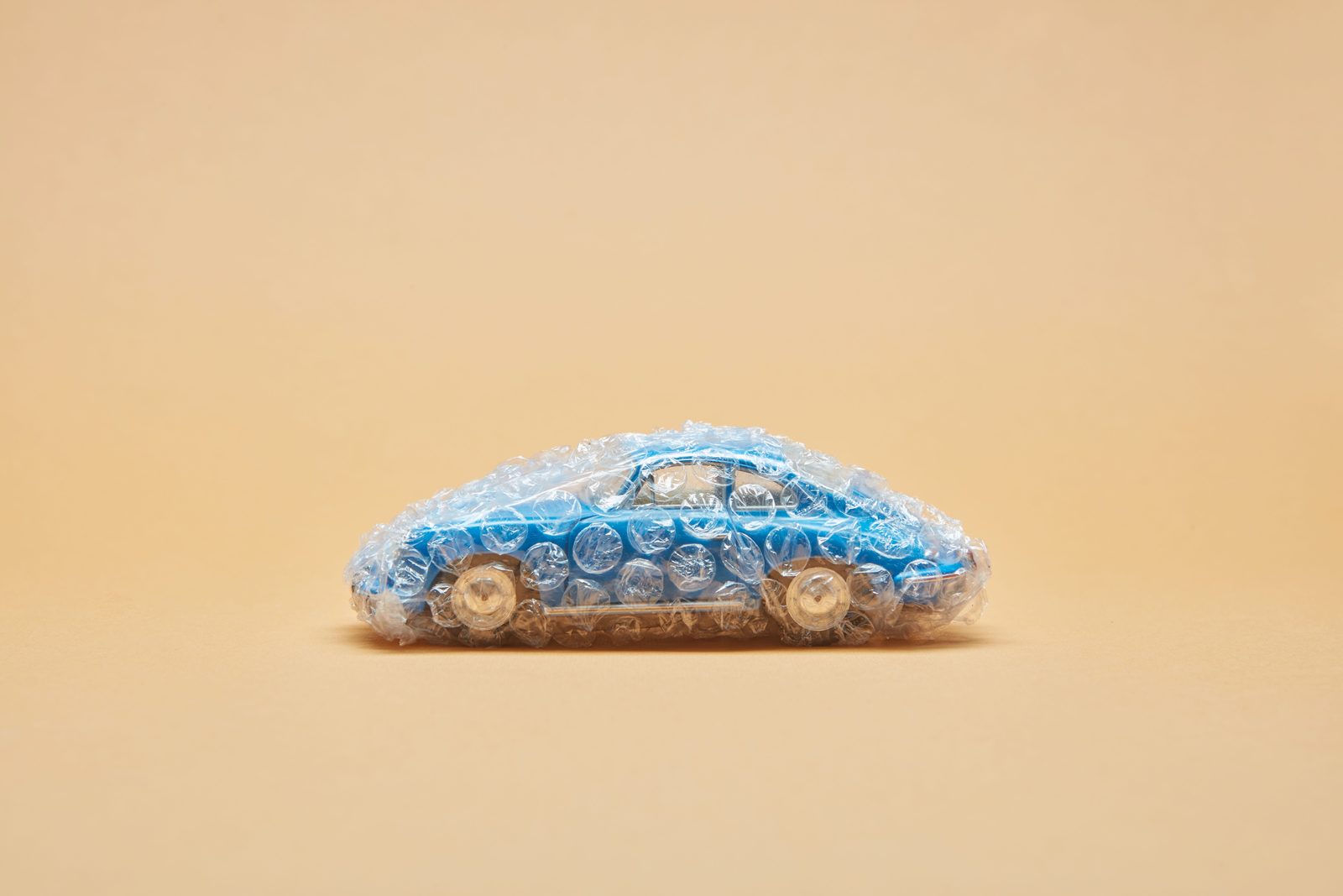 Blue toy car wrapped in bubble wrap against a beige background, minimalist concept.