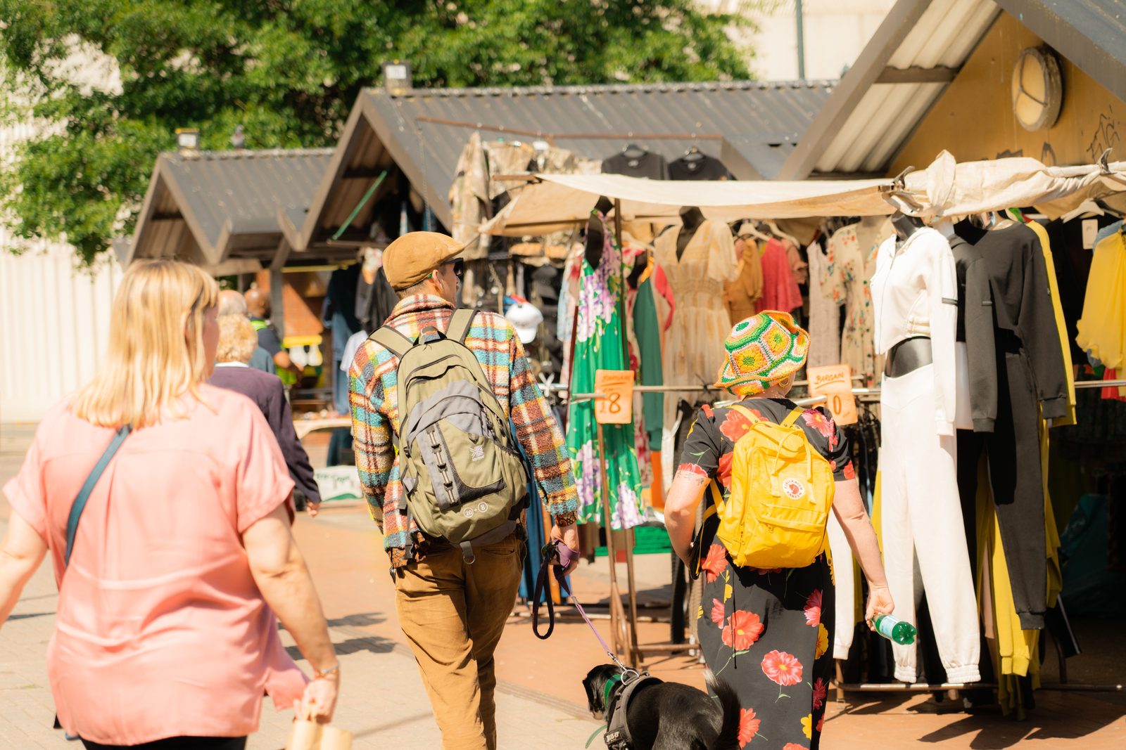 A bustling street market scene with people browsing clothes under sunny skies.