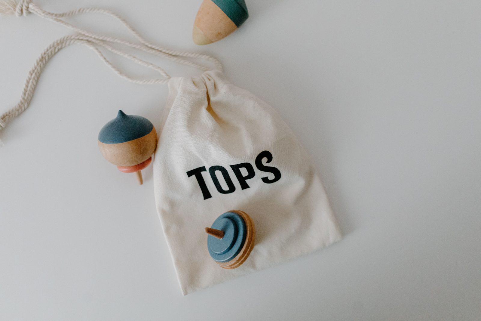 A minimalist photo of wooden spinning tops and a cloth bag labeled 'Tops'. Perfect for toy and lifestyle themes.
