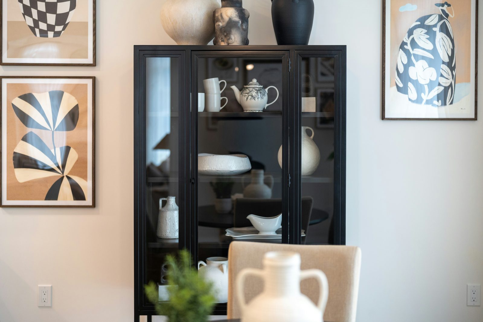 Black glass cabinet displaying decorative vases and artwork